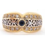 Two-tone yellow metal filigree fronted design ring, centring a small sapphire and highlighted with