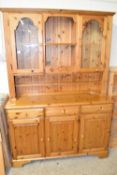 MODERN THREE DOOR VARNISHED PINE DRESSER WITH GLAZED CABINET ABOVE, WIDTH APPROX 132CM