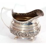 Georgian silver cream jug of oval form, ribbed with later embossed body, supported on four ball