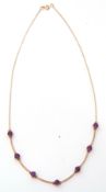 Modern amethyst necklace featuring seven round faceted amethysts, joined by curved bar links to a