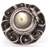 White metal filigree poison ring, the hinged mother of pearl lid opening to a vacant reservoir,