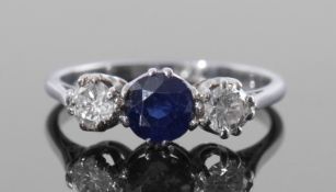 Precious metal sapphire and diamond three stone ring, the central round cut faceted sapphire flanked