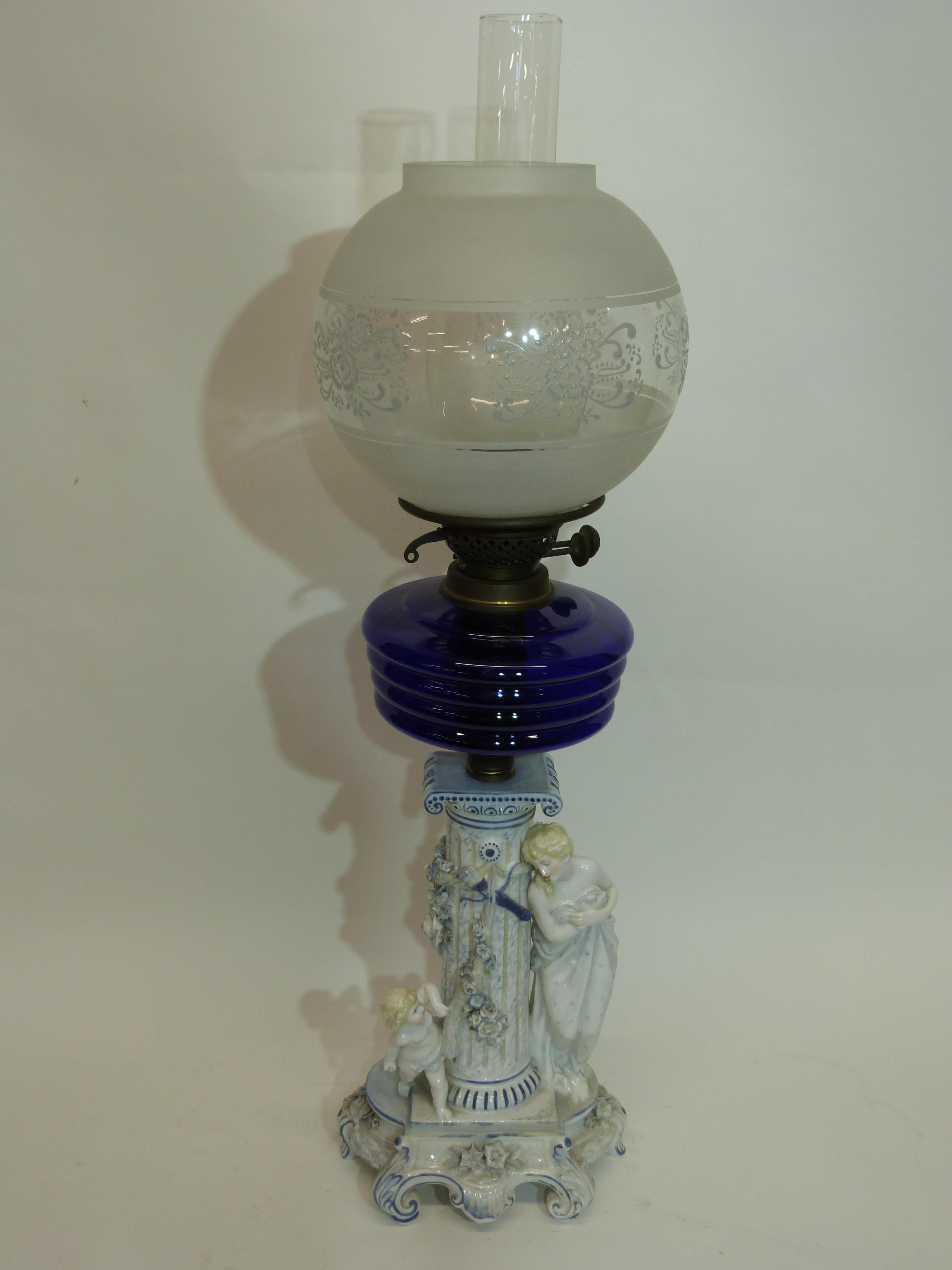 Oil lamp with blue glass reservoir below a white glass floral shade, supported by a porcelain column