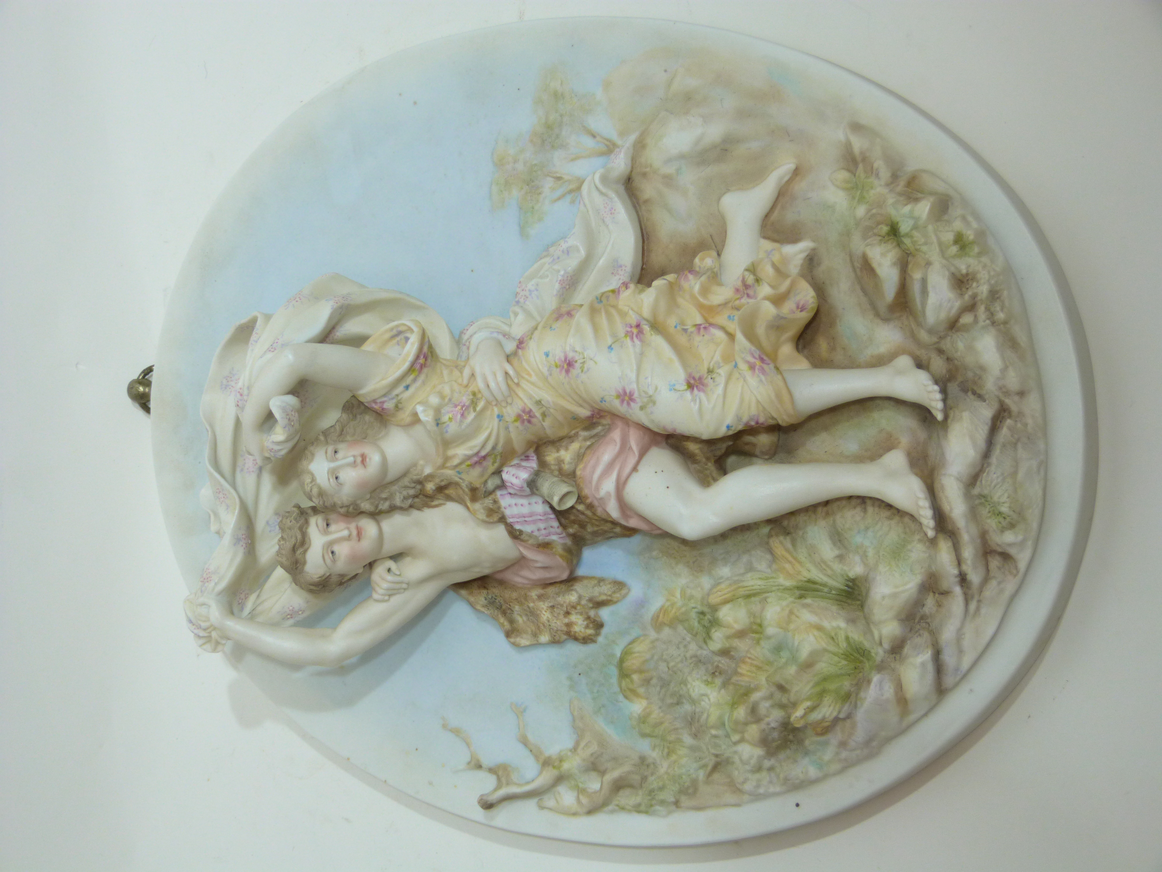 Oval porcelain plaque modelled in relief with two figures against a floral background, 23cm long