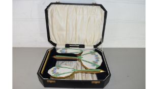 CASED FOUR PIECE DRESSING TABLE BRUSH AND MIRROR SET, THE BACKS DECORATED WITH FLORAL ENAMELLED