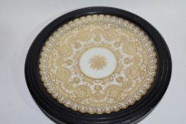 Wall plate with a gilt design encased in a wooden and glazed mount, 28cm diam