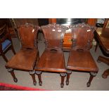 Set of three Georgian mahogany hard seated hall chairs, the backs with foliate carved decoration