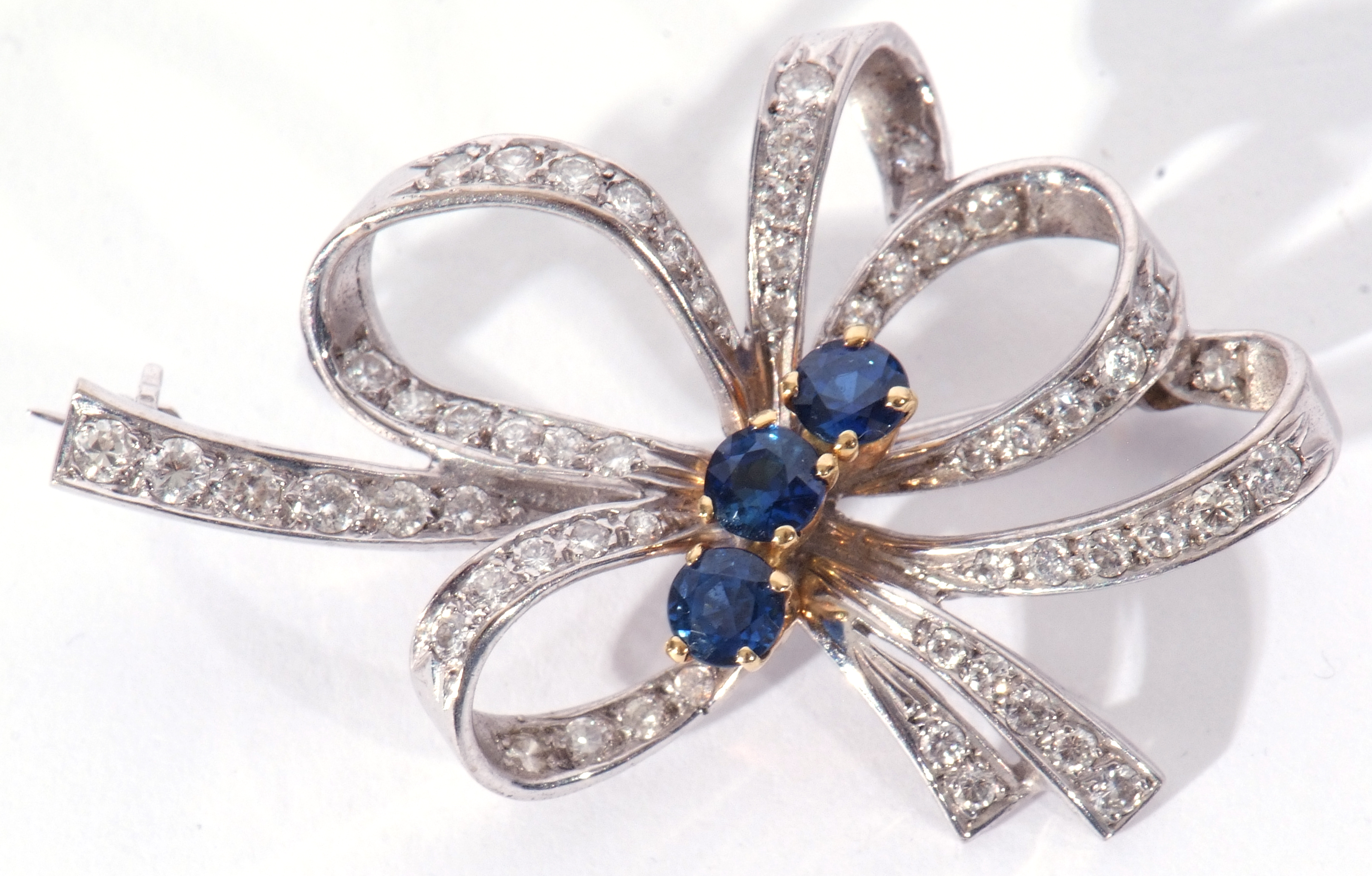 18ct white gold, sapphire and diamond brooch, a tied ribbon design centring three round cut small - Image 2 of 4