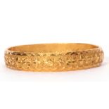 A high-grade yellow metal solid cast bangle of circular form, chased and engraved with a