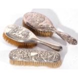 Group of three silver backed dressing table hand brushes comprising two brushes with cherub