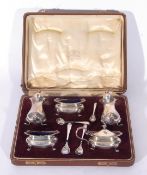 George V silver cased condiment set comprising two baluster pepper pots, two salt pots with blue
