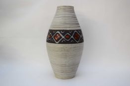 Large vase with ribbed design and central panel with red and white design on a dark grey background,