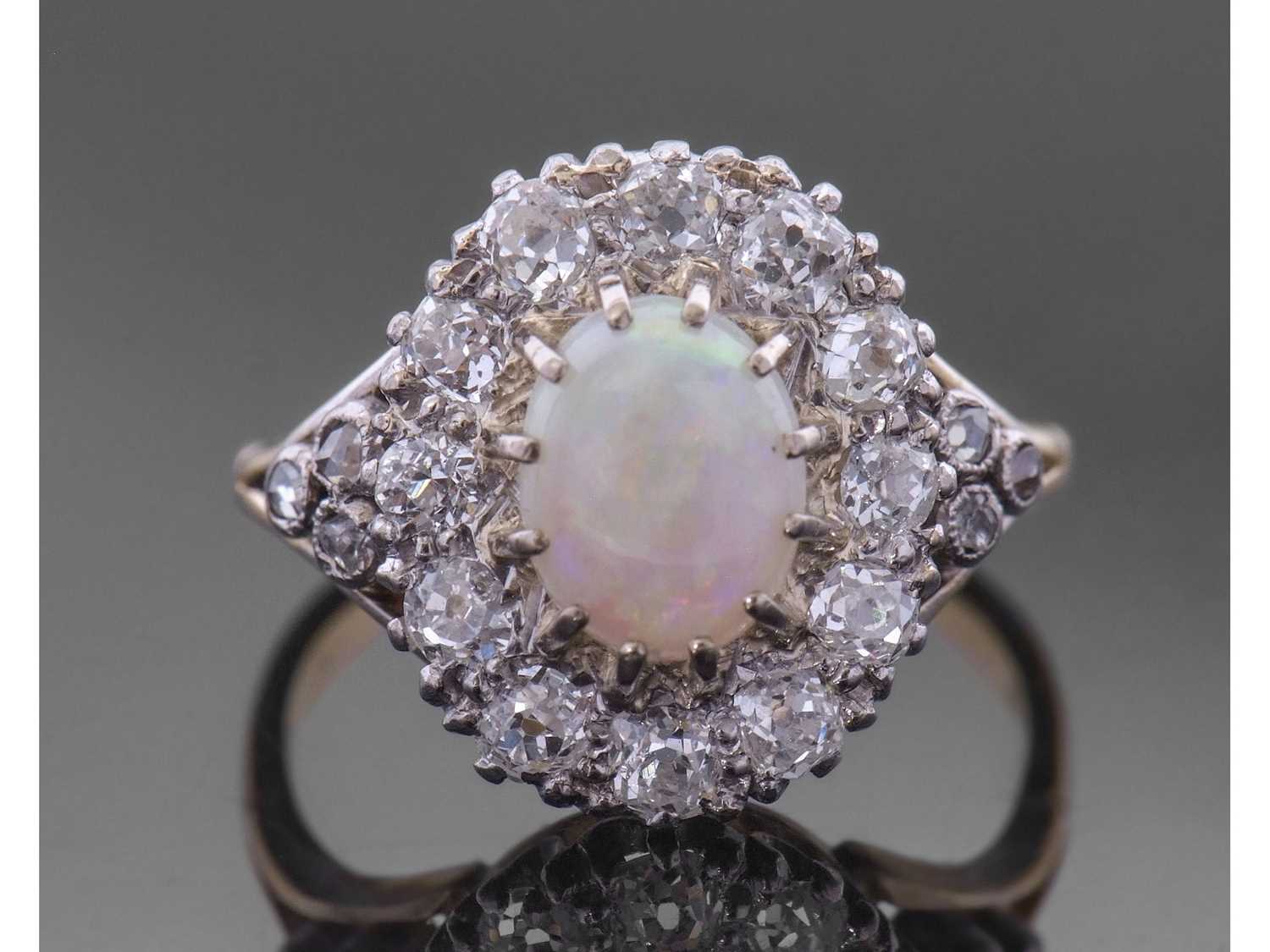 Opal and diamond cluster ring centring an oval shaped cabochon opal, multi-claw set and raised above