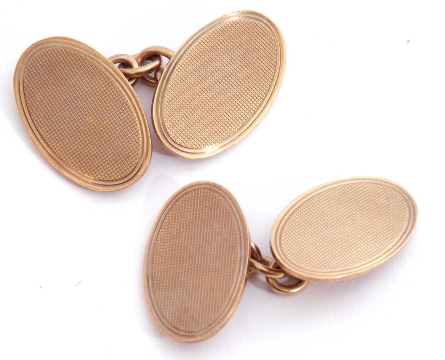 Pair of 9ct gold cuff links of oval shape, each panel with engine turned decoration, chain