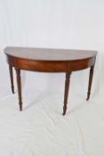 Georgian mahogany demi-lune hall table raised on four turned legs with casters, 126cm wide