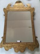 An early C18th gilded carved wood wall mirror with shaped and scrolling ears and finials. The oblong