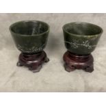 Pair of C19th/20th Chinese engraved green stone cups, wood stands. (2)