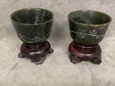 Pair of C19th/20th Chinese engraved green stone cups, wood stands. (2)