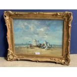 Gilt framed oil on board painting of a Victorian beach gathering with beach huts & boats offshore.