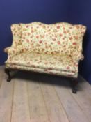 Early C20th upholstered winged settee with polished mahogany base & carved cabriole legs to ball &