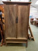 A teak style cupboard on stand, with the cupboard doors opening to reveal shelves and drawers 173 cm