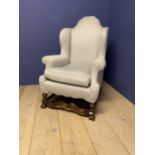 A large grey upholstered wing arm chair, with a Jacobean style wooden cross stretcher below, to