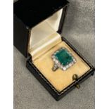 A platinum diamond and emerald ladies dress ring, central 5 ct emerald in 8 claw setting, with a