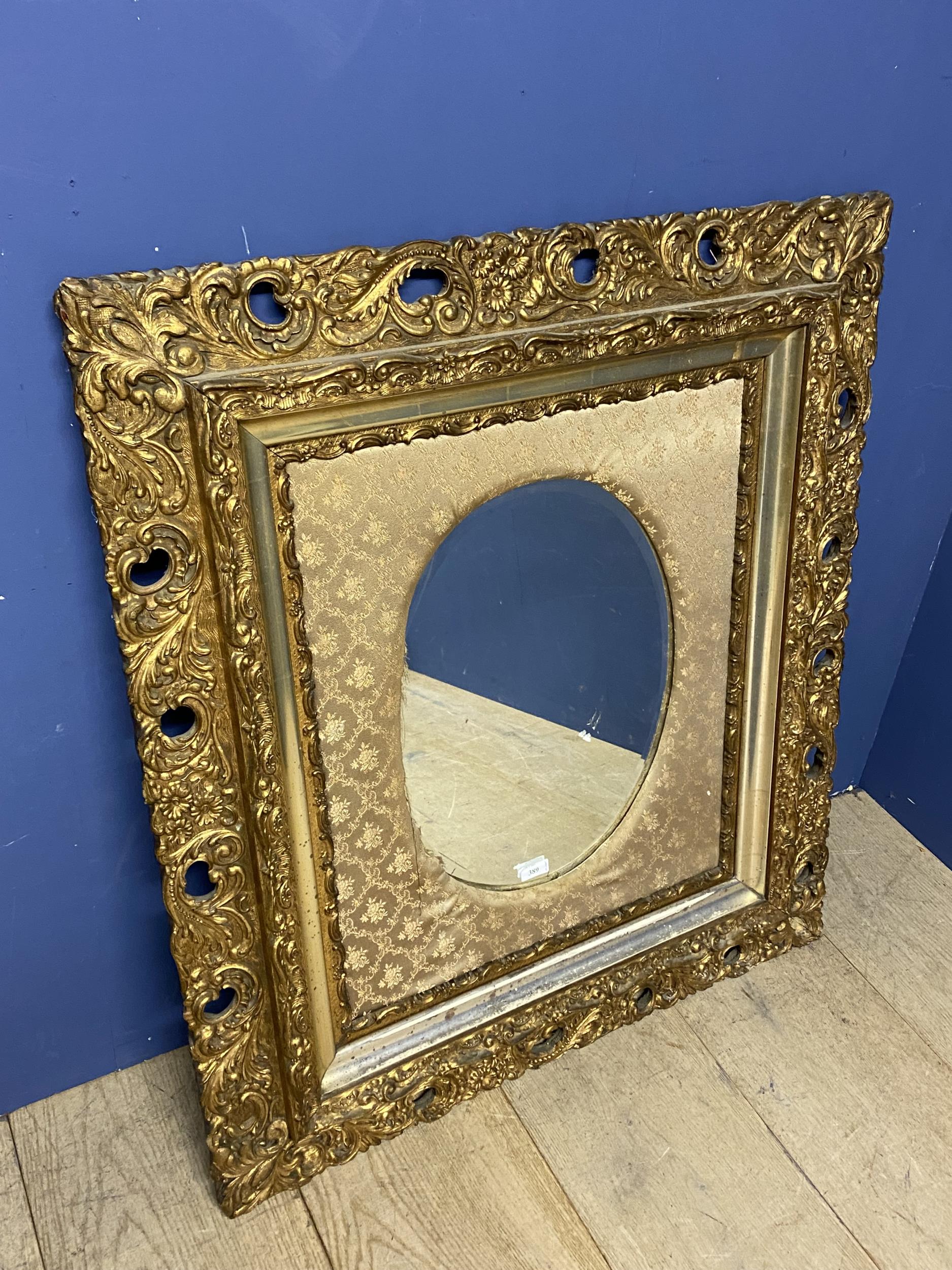 A decorative square framed, oval wall mirror, set withing a very ornately carved gilt frame and