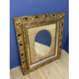 A decorative square framed, oval wall mirror, set withing a very ornately carved gilt frame and