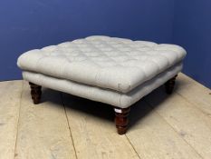 A grey upholstered square stool on wooden legs