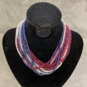 A triple stand necklace of cabochon ruby, sapphires and seed pearls, on a pearl set 14ct white