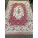 A needlepoint rug, with cream central medallion and borders, and pink central ground with garland