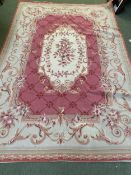 A needlepoint rug, with cream central medallion and borders, and pink central ground with garland