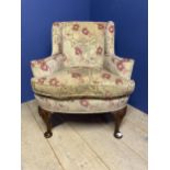 A floral upholstered arm chair raised on wooden legs to pad feet