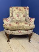 A floral upholstered arm chair raised on wooden legs to pad feet