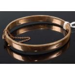 A gilt metal half engraved oval hinged bangle, having box clasp and safety chain, width 8.0mm,