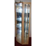 A contemporary beech and glazed freestanding single door corner display cabinet, having glass