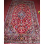 A Persian woollen Tabriz rug, having a red ground decorated with scroll flowers and foliage within