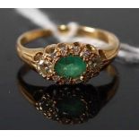 An 18ct gold, emerald and diamond cluster ring, the claw set oval cut emerald in a surround of round