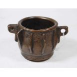 A bronze mortar, of squat circular form, having one pierced handle, with raised fin-like banding,