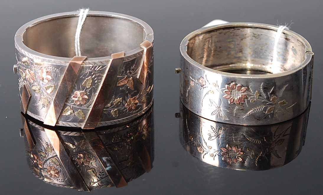 Two white metal oval hinged bangles, each with engraved gilded floral detail, w.24 and 32mm, inner