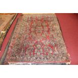 A Persian woollen red ground rug, decorated with flowers and foliage within trailing tramline