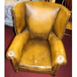 An early 20th century tan leather and studded upholstered barrel back scroll armchair raised on