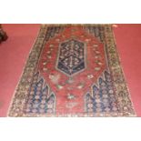 A Turkish woollen rug, the rust coloured field decorated with stylised motifs within trailing