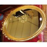 A contemporary gilt wood oval wall mirror, having ribbon floral surmount and gadrooned outer edge,