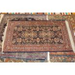 A Persian woollen rug, the blue ground decorated with scroll flowers and foliage within trailing