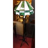 A black painted wrought iron standard lamp, having a Tiffany style coloured lead glass dome shade,