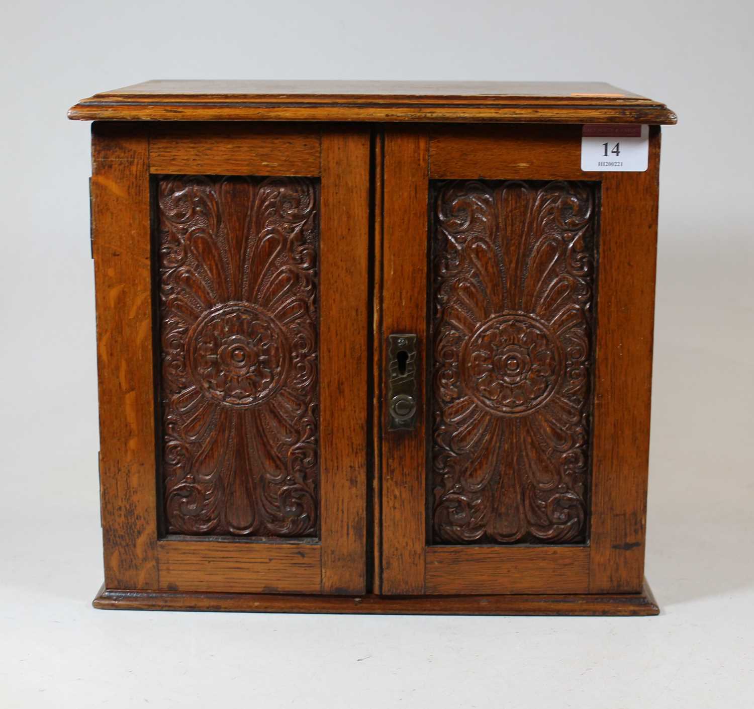 An Edwardian oak smokers cabinet, having a hinged lid above a pair of panelled doors, opening to