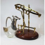 A brass framed decanting cradle with rotating action on a mahogany plinth, together with a novelty