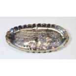 A white metal oval dish of scalloped oval form relief decorated with a figure and goat within